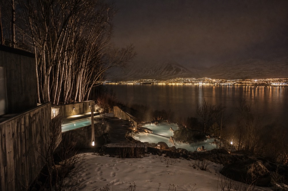A city-edge geothermal lagoon at night with urban lights glowing on the horizon
