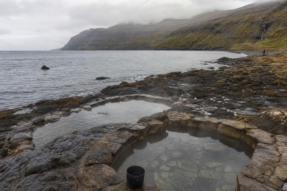 Steaming stone-lined pools on a hillside above a narrow fjord