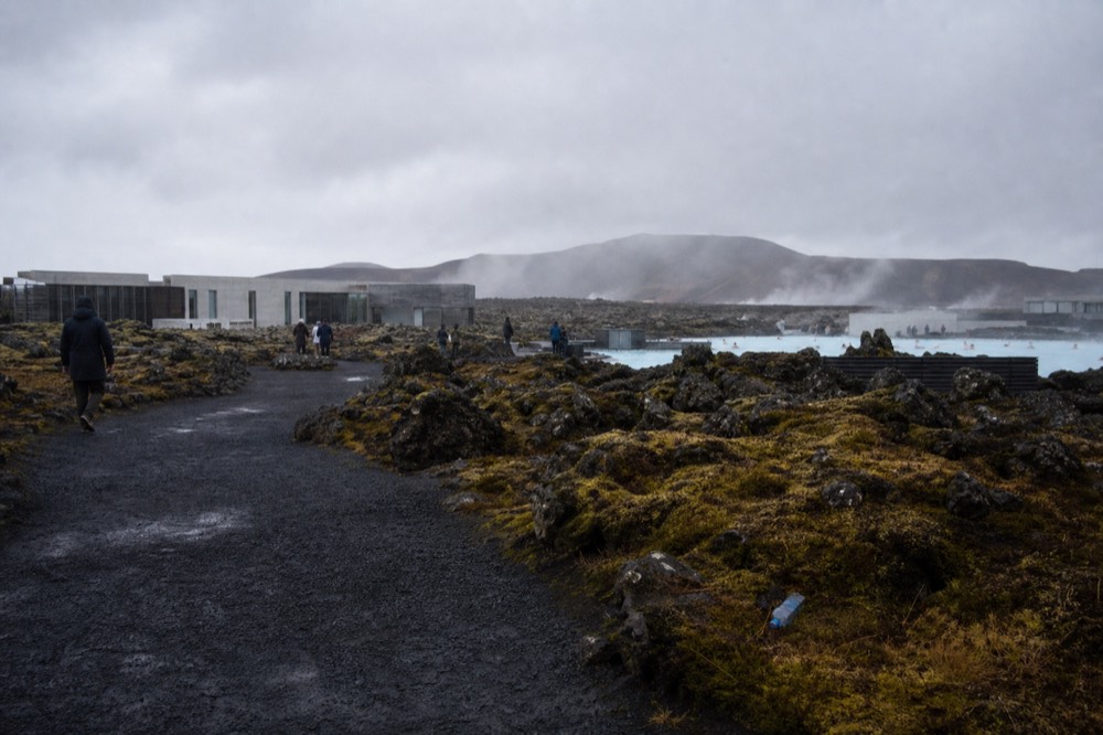 A wide volcanic plain with steaming vents and low ridges under a grey sky