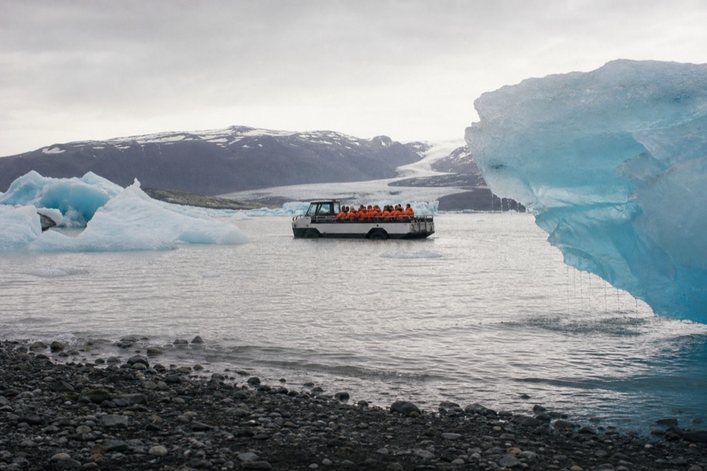 An amphibious boat carrying passengers between icebergs on a grey glacial lagoon