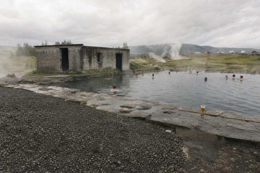 A steaming natural hot pool surrounded by gravel and small geothermal vents
