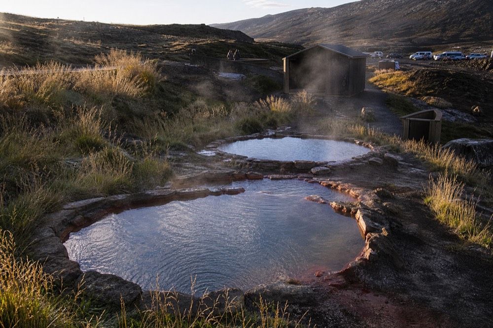 Three side-by-side geothermal pools of different sizes on a dark hillside