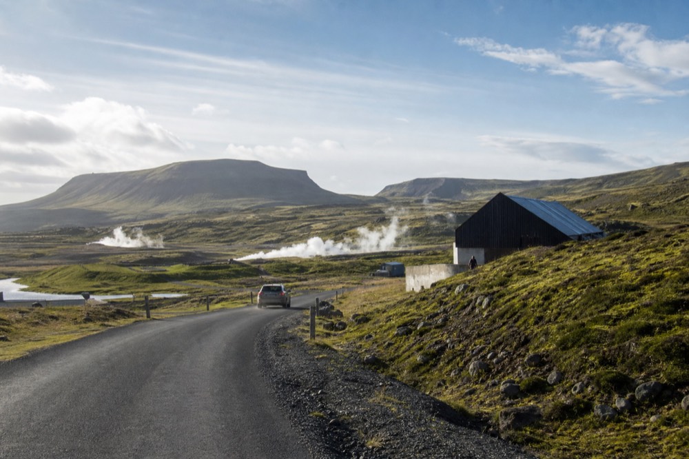 A paved rural road curving through green hills with distant mountains
