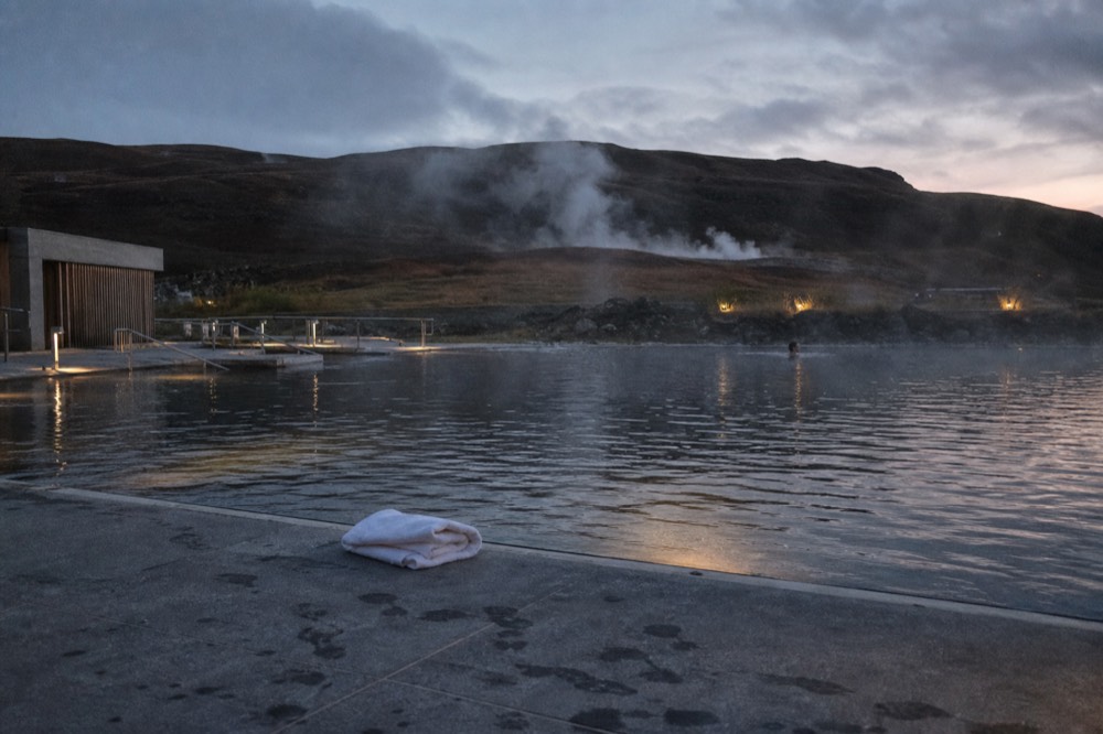 A calm geothermal pool at dusk with warm light reflecting on the water