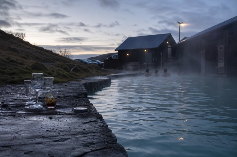 Still water in a geothermal pool at dusk with steam drifting across the surface