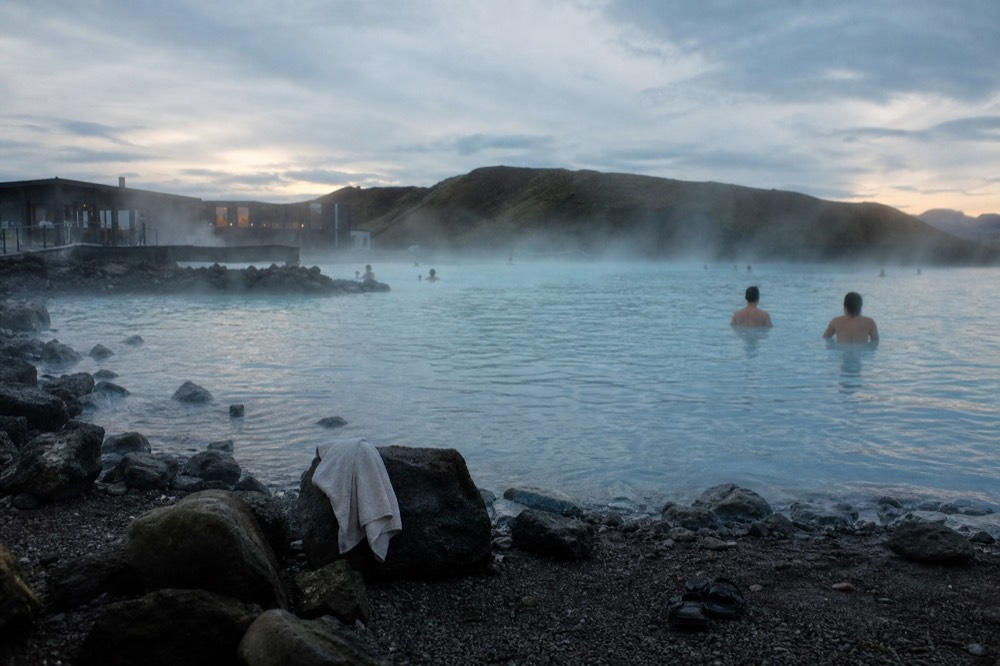 A wide geothermal lagoon with steam drifting across turquoise water and dark lava fields beyond