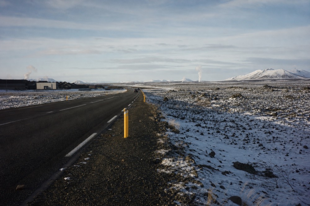 A long empty road crossing a volcanic plain with distant steaming vents