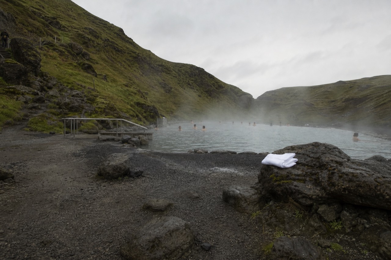 Steam rising from a geothermal lagoon beside a mossy hillside in South Iceland