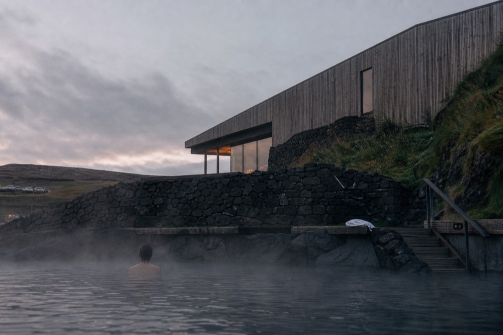 Wooden-clad building above a steaming lagoon at dusk