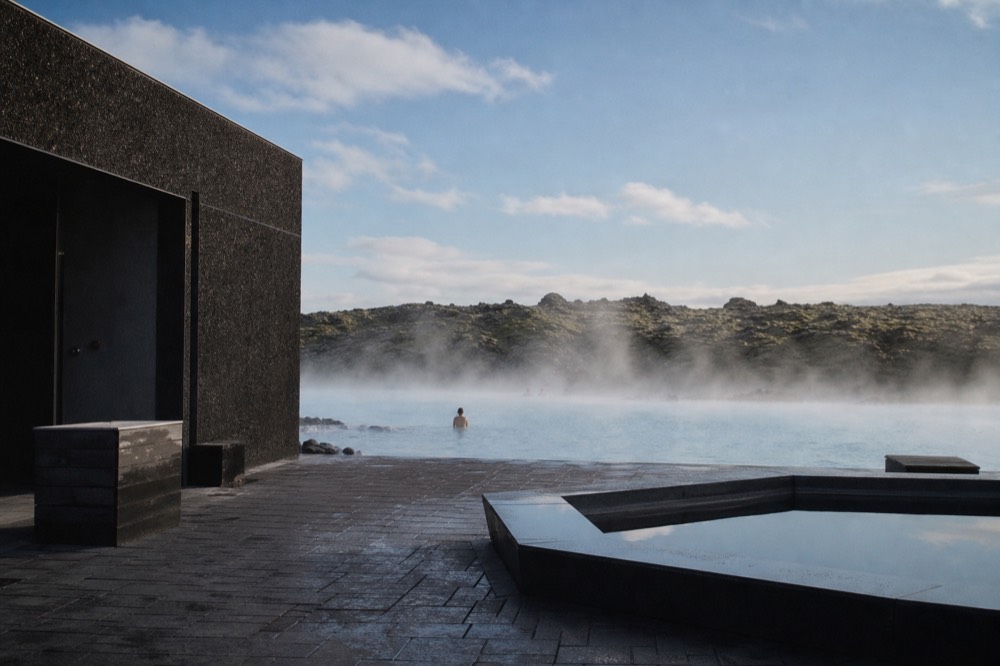 A minimalist spa building of dark stone overlooking a steaming geothermal lagoon