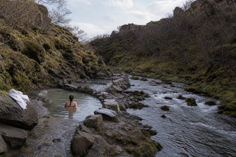 A series of small stone-lined geothermal pools terraced into a hillside above a fjord