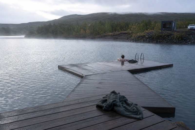 A geothermal lagoon in east and southeast Iceland, steaming water beside a glacial landscape with floating icebergs and dark sand.