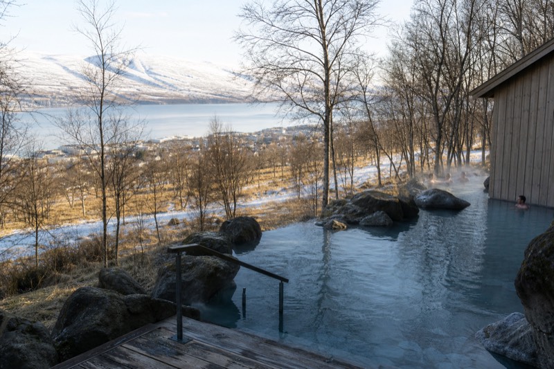 A geothermal bathing lagoon in north Iceland near Akureyri, steam drifting over the water with snowy mountains in the distance.